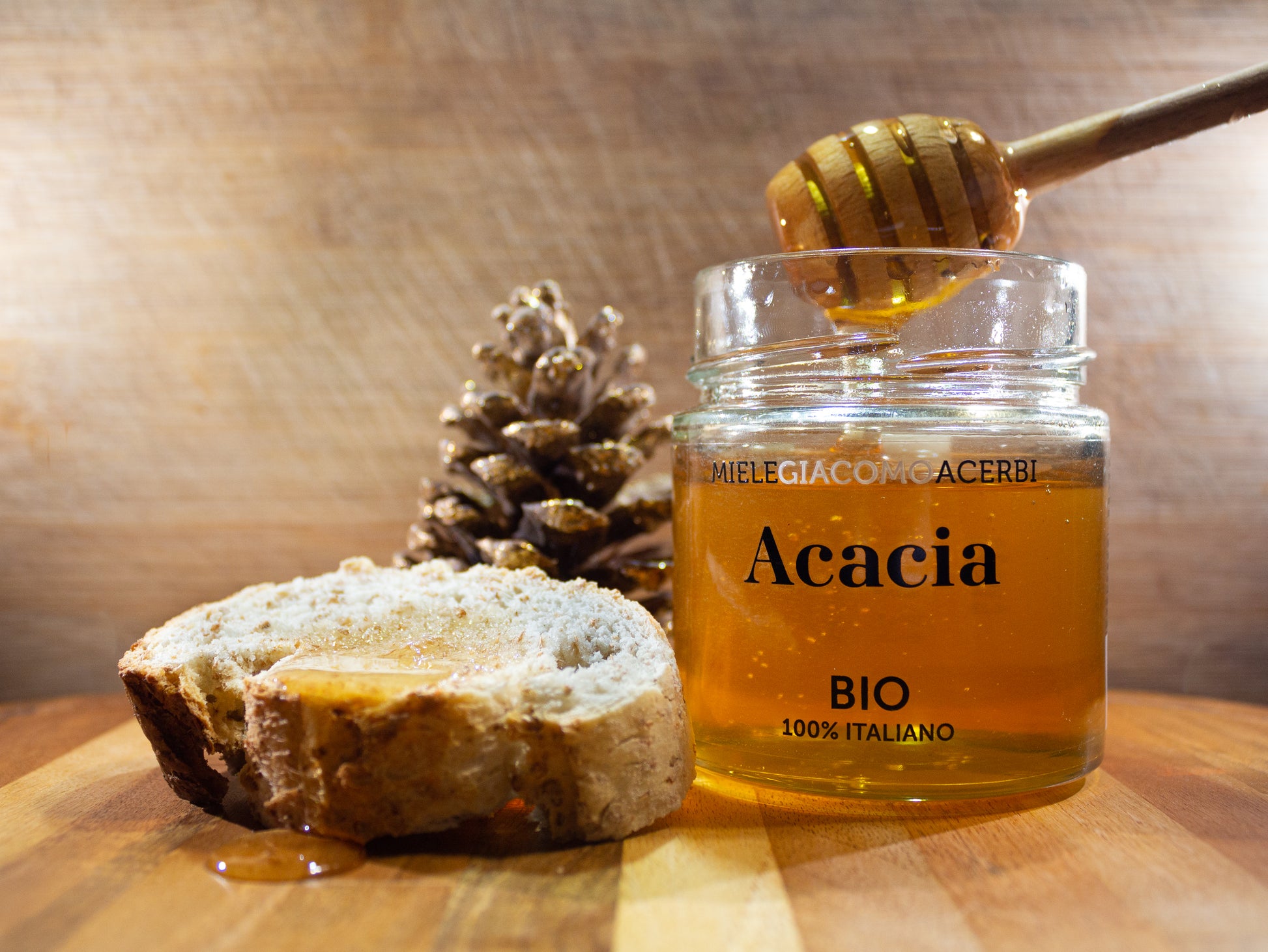 Miele d'Acacia con ambientazione in legno e pigne, spalmato su una fetta di pane