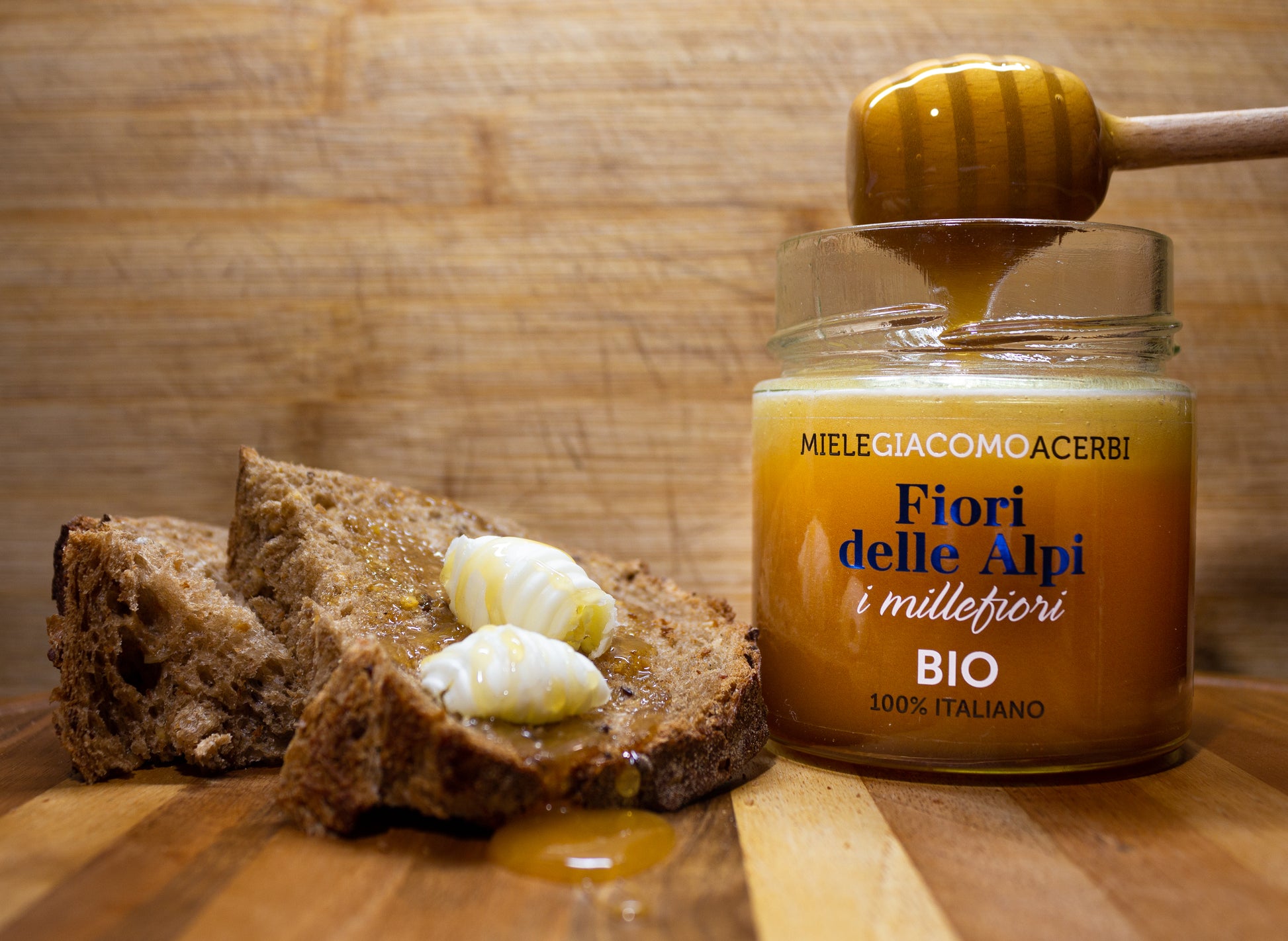 Miele millefiori Fiori delle Alpi con ambientazione in legno, abbinato con pane integrale e noci di burro